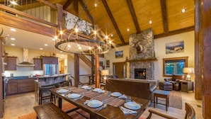 Une vaste salle à manger avec une longue table en bois dressée pour le repas, une cheminée en pierre et un escalier menant à un niveau supérieur.