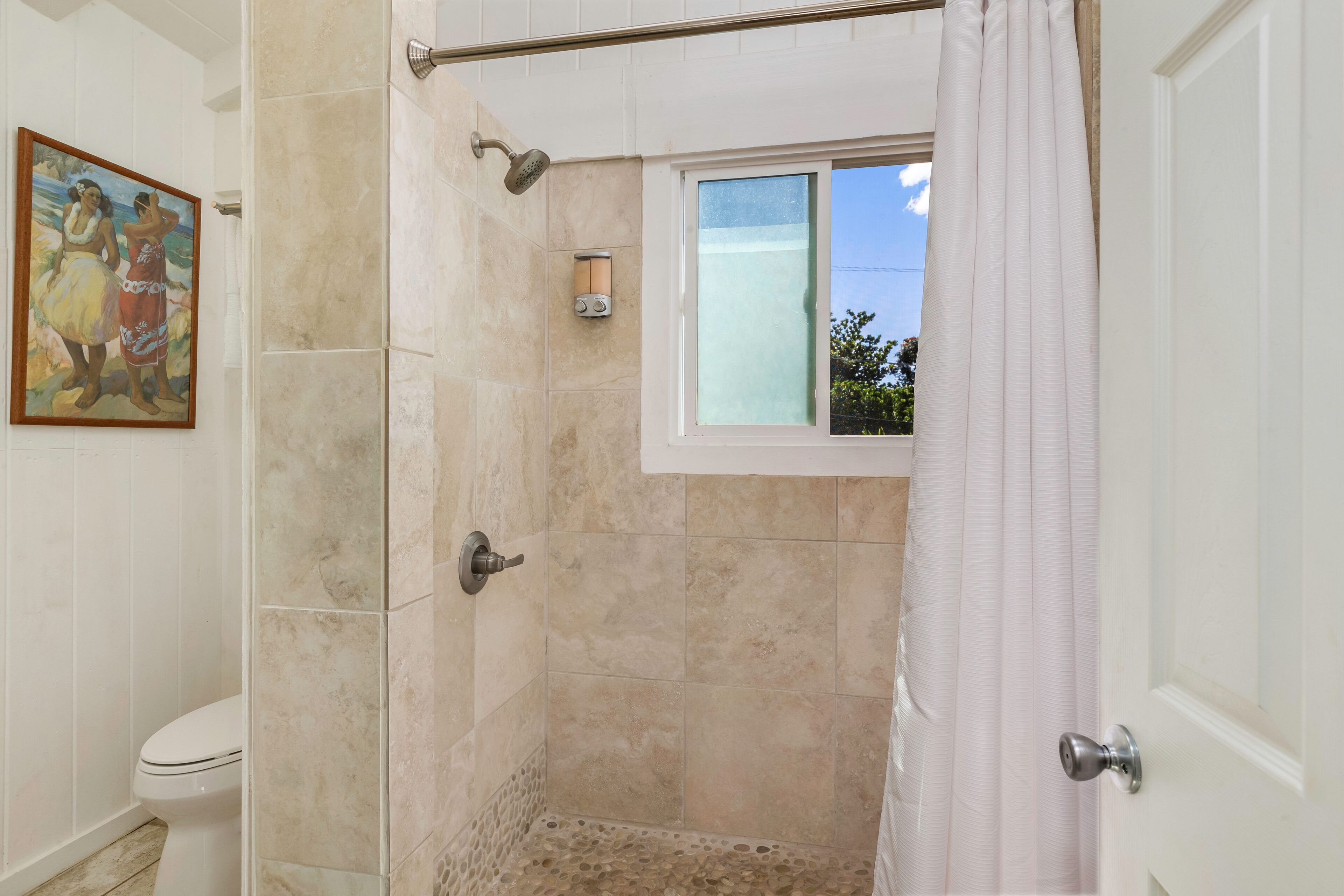 Un baño con ducha, inodoro y ventana con vista al cielo.