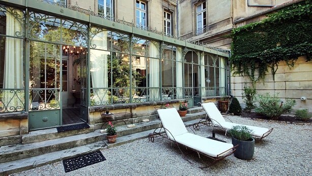 Ein Innenhof mit einem Wintergarten, Sitzgelegenheiten im Freien und einer Fassade aus Stein.