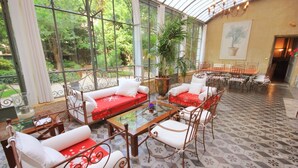 Ein Wintergarten mit Glasdecke, ausgestattet mit Sofas, Sesseln, einem Esstisch und einer großen Topfpflanze.