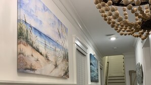 Un couloir orné d’un tableau représentant une plage, d’un escalier et d’un luminaire décoratif.