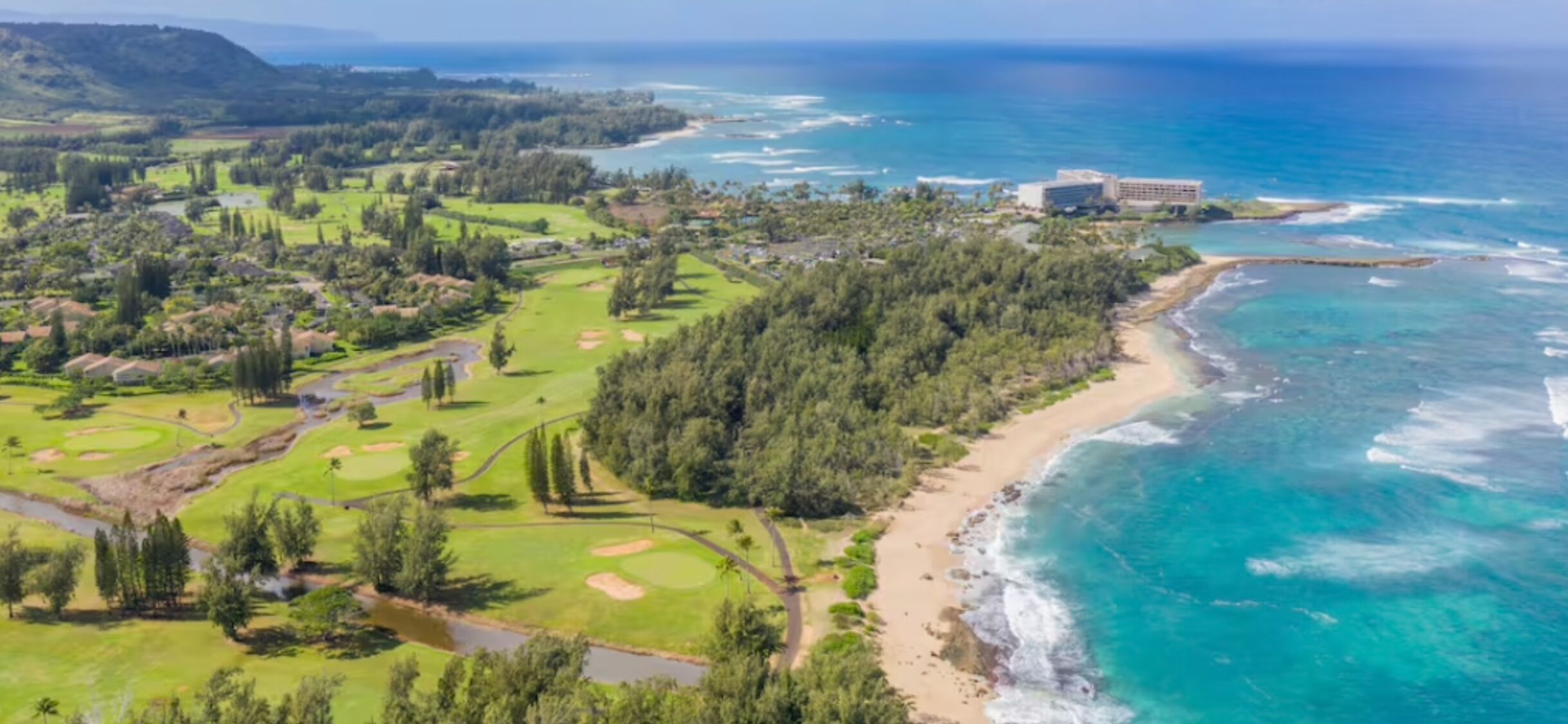 Un campo de golf costero con playa, océano y un edificio grande al fondo.