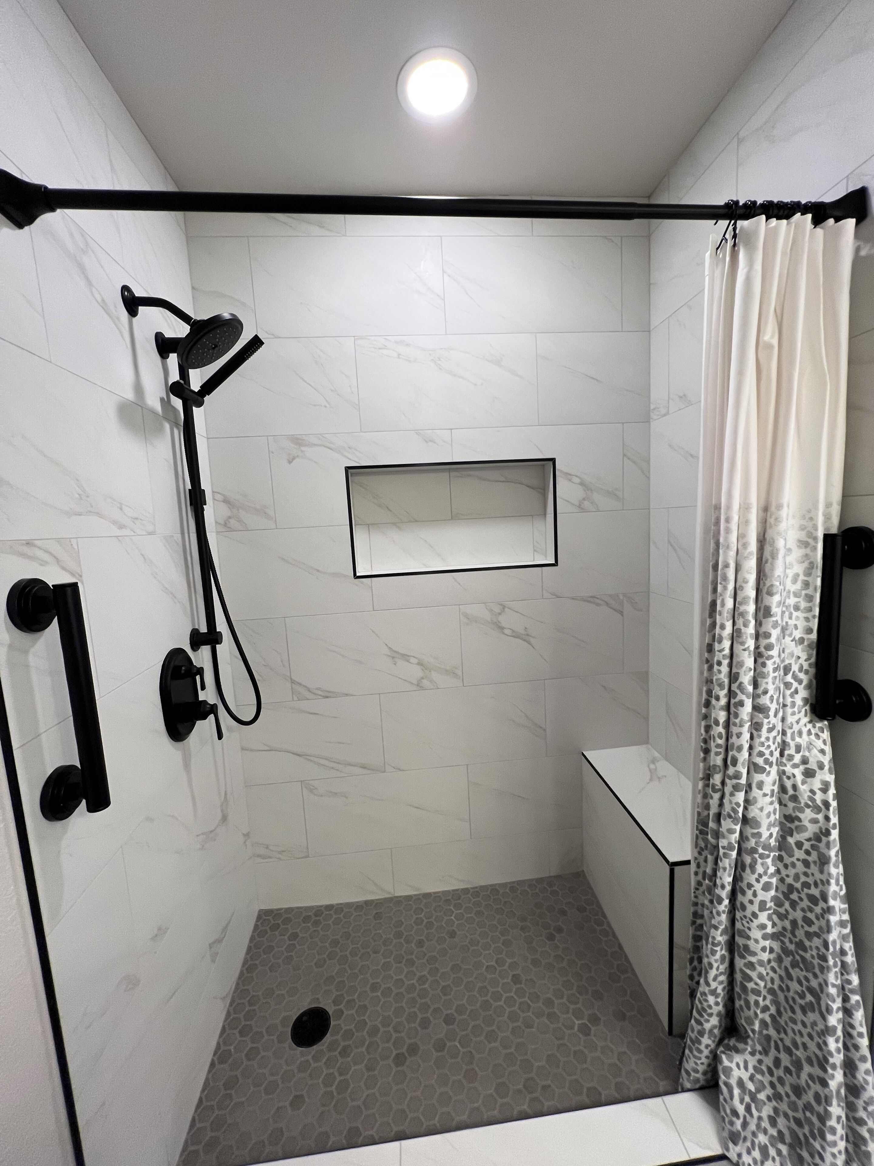 Zona de ducha con cabezal de ducha manual, estante rectangular y cortina de baño estampada.