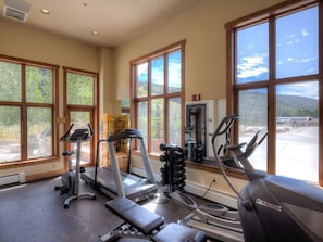 Ein Fitnessstudio mit Laufbändern, Crosstrainern und Gewichtbänken, große Fenster mit Blick auf Bäume und Berge.