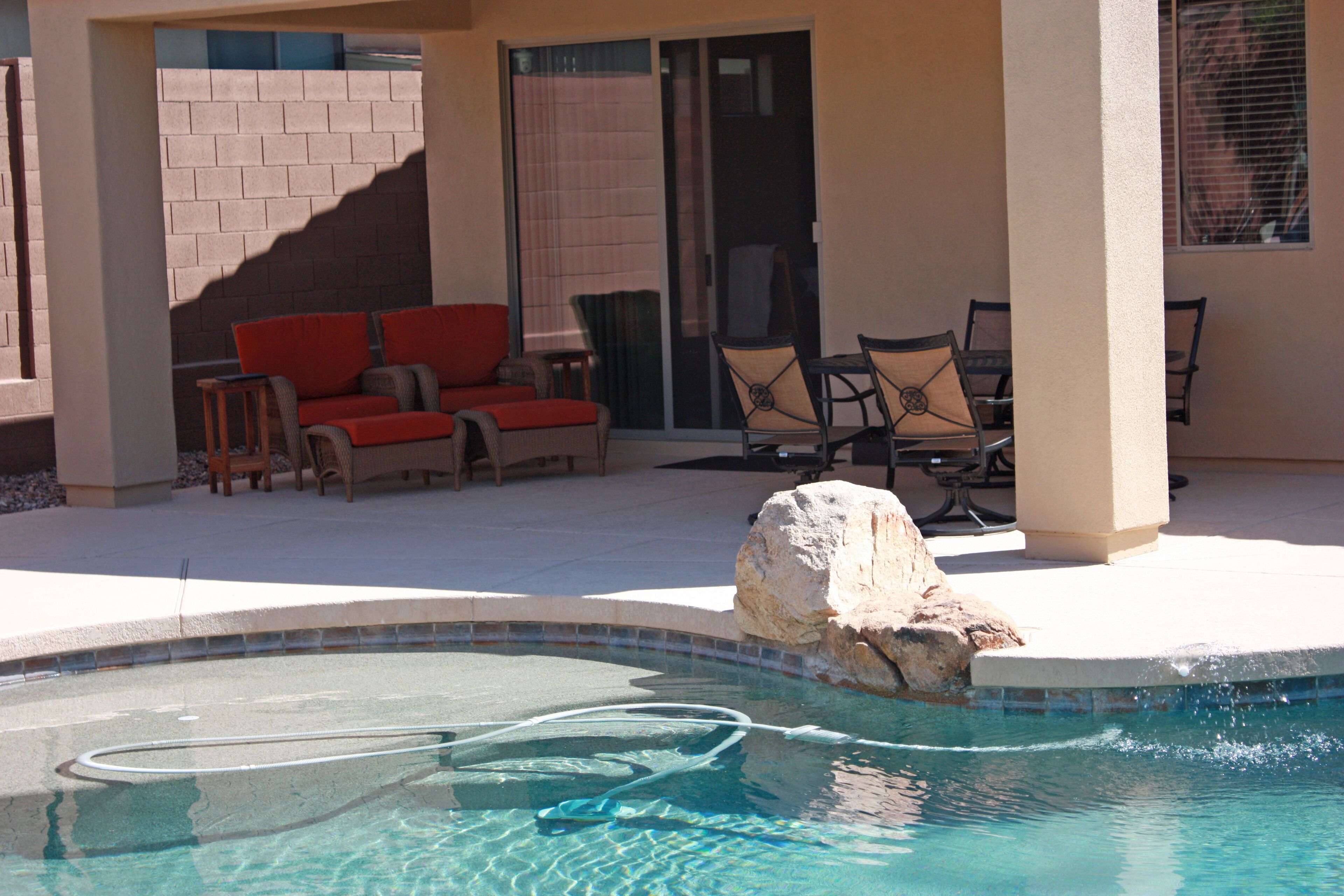 A swimming pool with a stone feature, a red sofa, and two chairs.