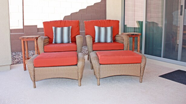 A wicker sofa set with red cushions and striped pillows, positioned on a patio with a glass door and a brick wall in the background. - Cozy private country club oasis with pool! (Anthem)