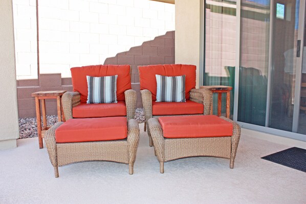A wicker sofa set with red cushions and striped pillows, positioned on a patio with a glass door and a brick wall in the background. - Cozy private country club oasis with pool! (Anthem)