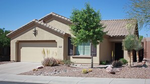 A residential house with a garage, a small tree, and desert landscaping. - Cozy private country club oasis with pool! (Anthem)