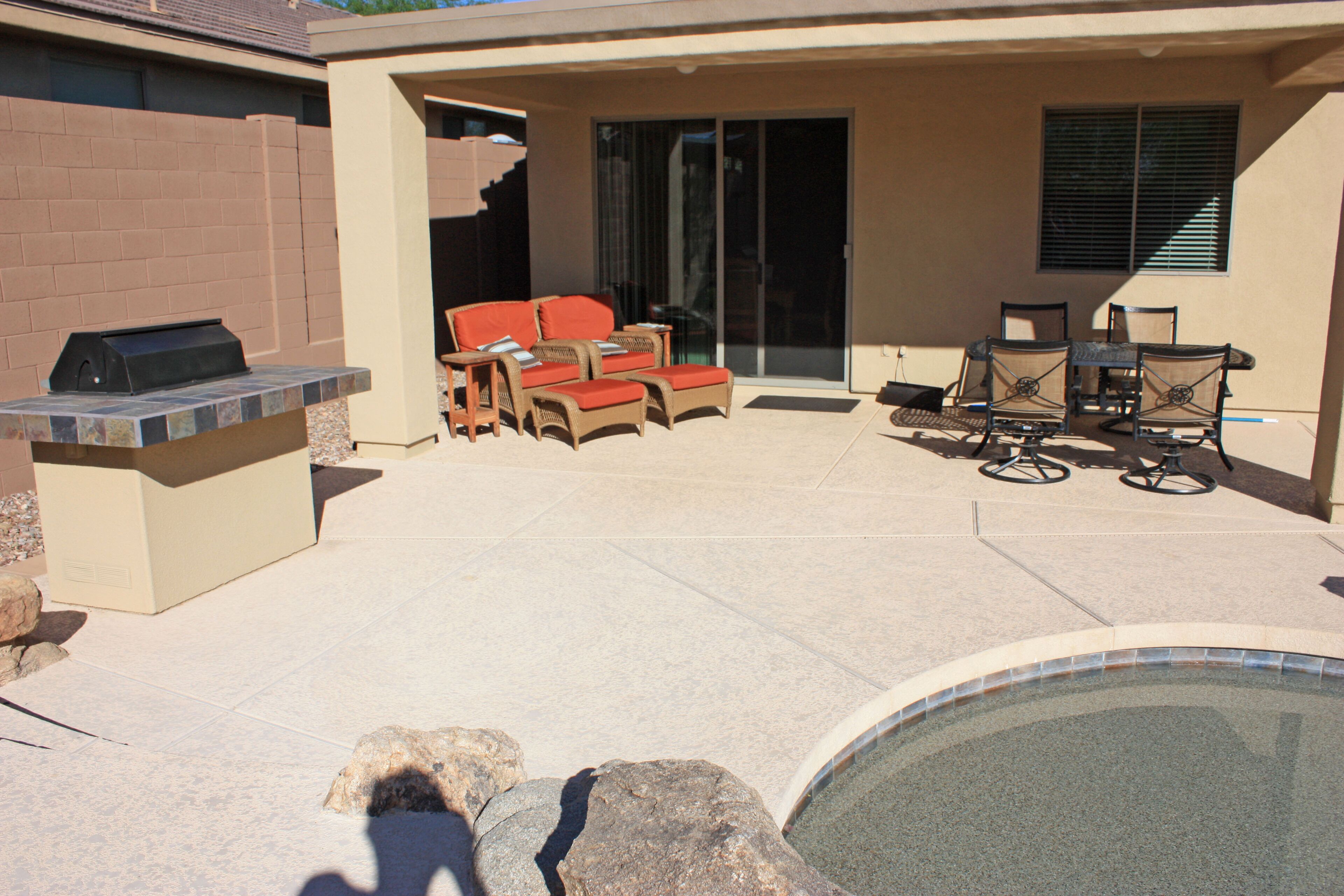 A covered patio with a barbecue, outdoor seating, and a swimming pool.