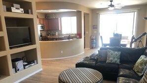A living room with a black leather sofa, a striped ottoman, and a flat-screen TV on a shelf. - Cozy private country club oasis with pool! (Anthem)