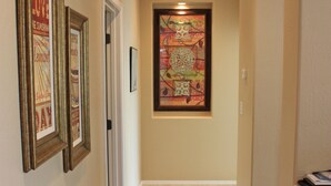A hallway with beige walls, a tiled floor, and framed artwork on the walls. - Cozy private country club oasis with pool! (Anthem)