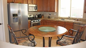 A kitchen with wooden cabinets, stainless steel appliances, a dining table with chairs, and a window with blinds. - Cozy private country club oasis with pool! (Anthem)