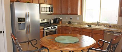 A kitchen with wooden cabinets, stainless steel appliances, a dining table with chairs, and a window with blinds.