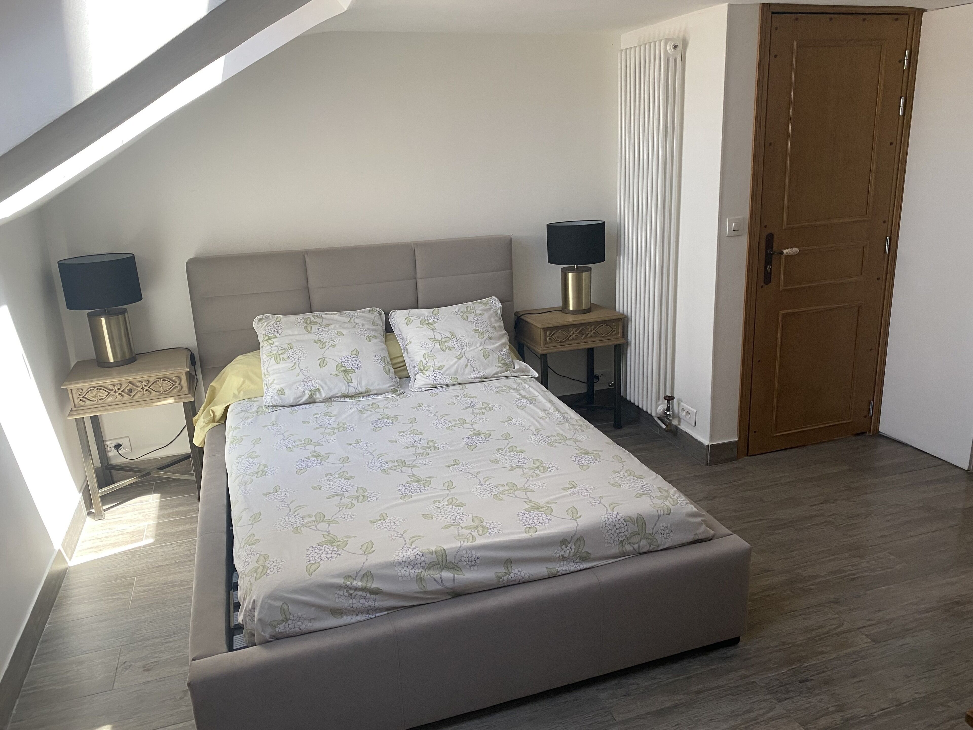 Een slaapkamer met een bed, twee nachtkastjes met lampen, een houten deur en een raam met jaloezieën.