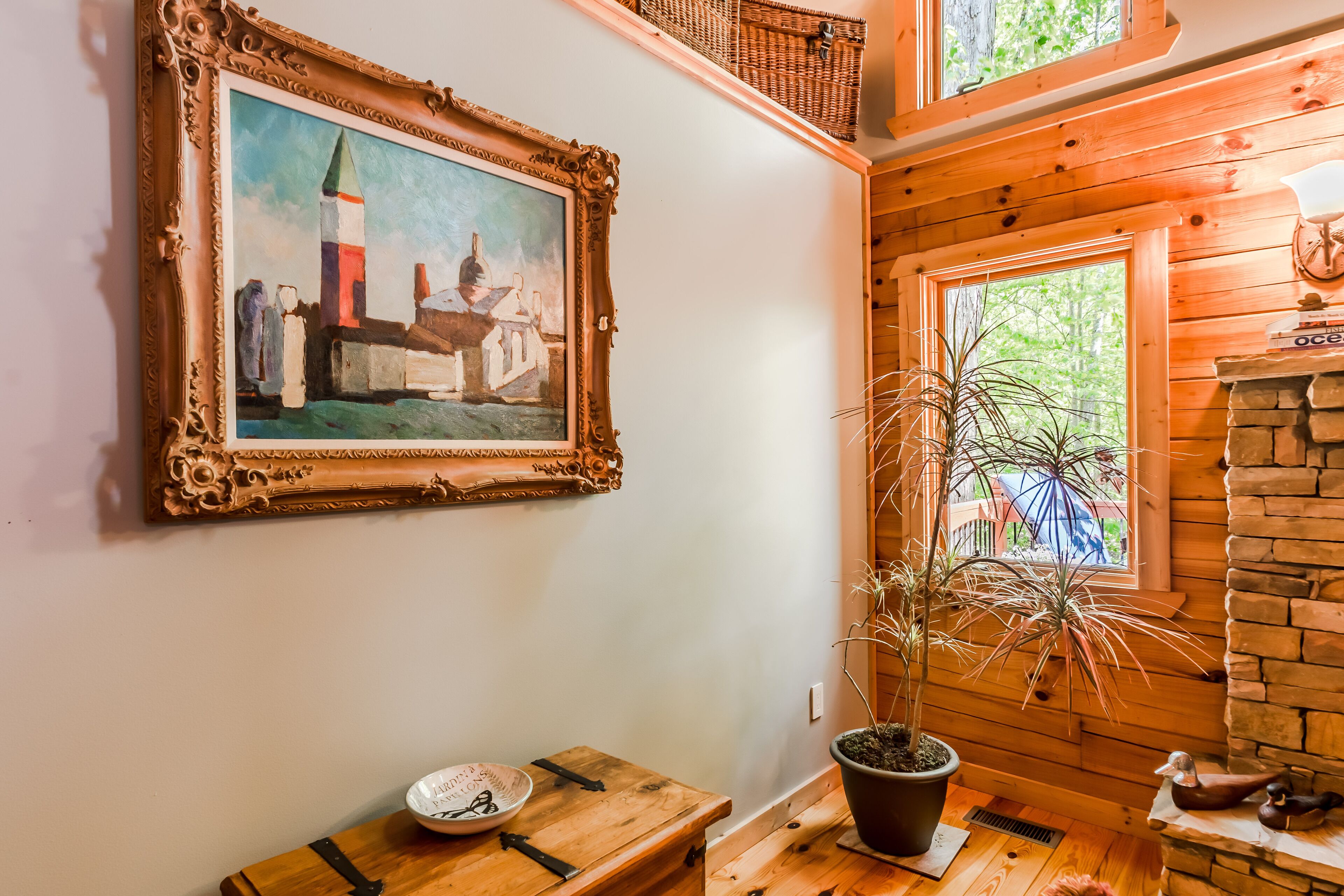 Un intérieur rustique agrémenté d’un tableau encadré, d’une table en bois sur laquelle se trouve un bol, d’une plante en pot et d’une cheminée en pierre.