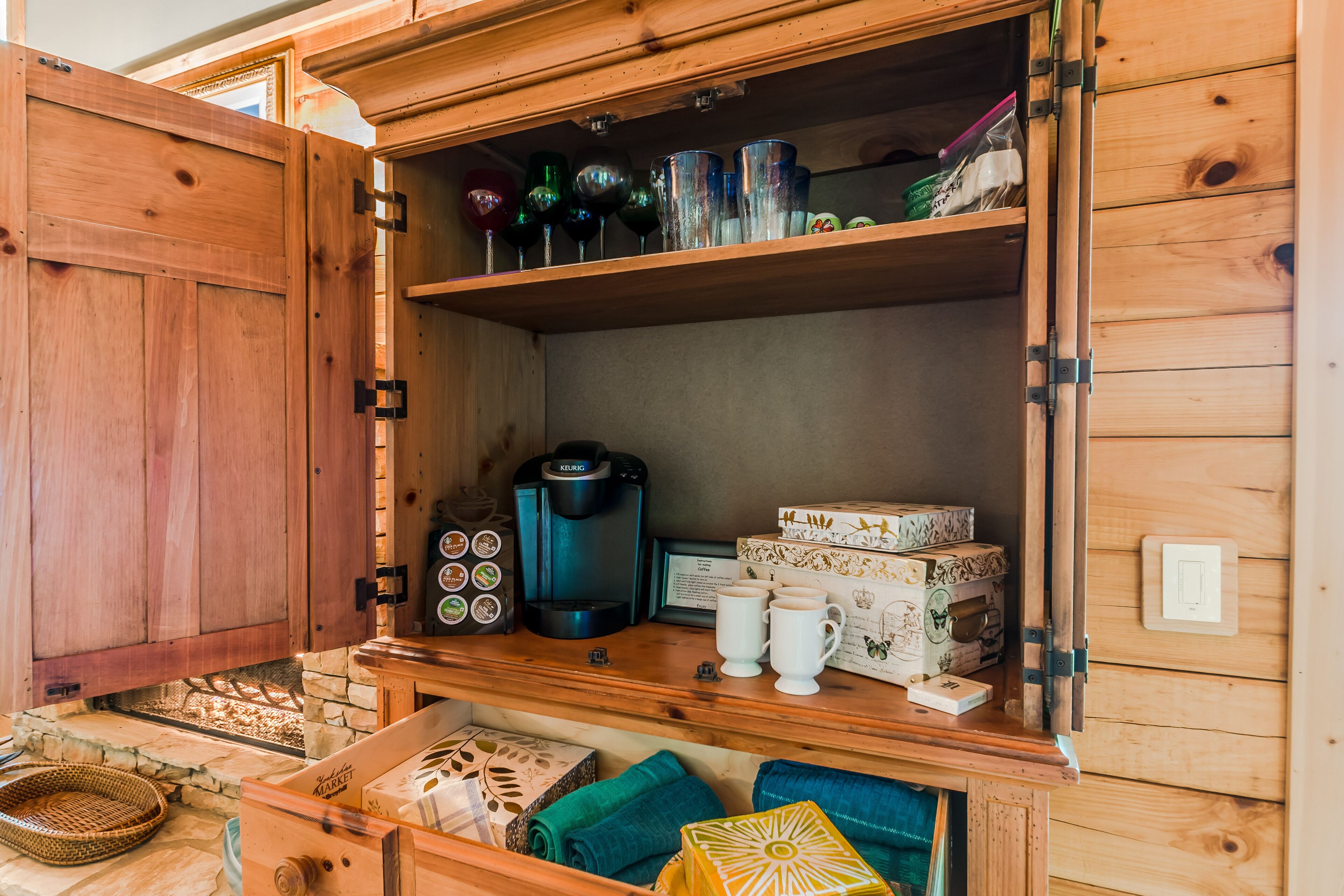 A wooden cabinet with shelves containing various items including a coffee maker, mugs, and boxes.
