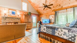 A cozy log cabin interior with a fireplace, a large bed, a television, and a dining area. - ♨️Hot Tub🛏️King Bed🔥Fireplace 🍷Wineries🌲Oasis🥾Hike🌎Comfy🔥Fire Pit⛲Pond 🆒 (Dahlonega)