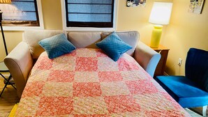 A bedroom with a bed covered in a floral quilt, a blue chair, and a lamp on a bedside table.