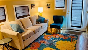 A living room with a beige sofa, a blue armchair, and a colorful floral rug.
