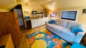 A compact living space with a kitchenette, a sofa with cushions, and a colorful floral rug.