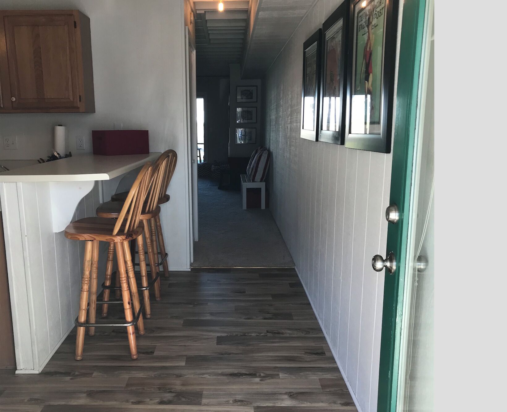 A narrow hallway with a kitchen area on one side, featuring a wooden counter and bar stools.