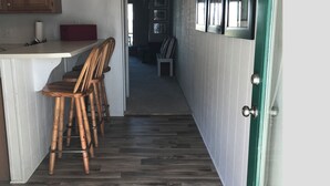A narrow hallway with a kitchen area on one side, featuring a wooden counter and bar stools.