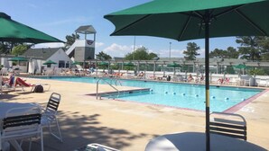 A swimming pool area with lounge chairs and umbrellas, a covered seating area, and a flag on a building in the background.