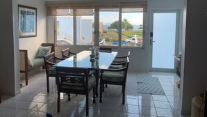 Un comedor con una gran mesa y sillas, un sofá, y vistas a una zona residencial a través de amplios ventanales.