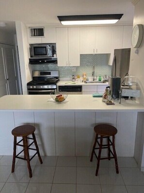 A modern kitchen with white cabinets, a central island with stools, a microwave, a stove, and a refrigerator. - Lovely, spacious upstairs condo at Crystal Cove, on Sapphire beach. (St Thomas)