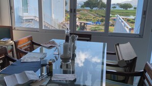 Un comedor con mesa de vidrio, sillas y vista a una zona residencial con casas y una masa de agua.