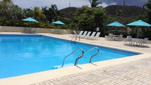 Una piscina con borde de azulejos, rodeada de sillas de descanso y sombrillas, con un paisaje montañoso al fondo.