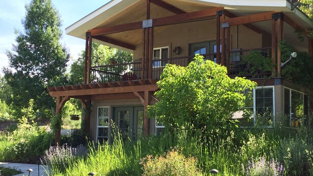 Een tweelaags huis met een overdekte veranda en een groot raam met uitzicht op een tuin.
