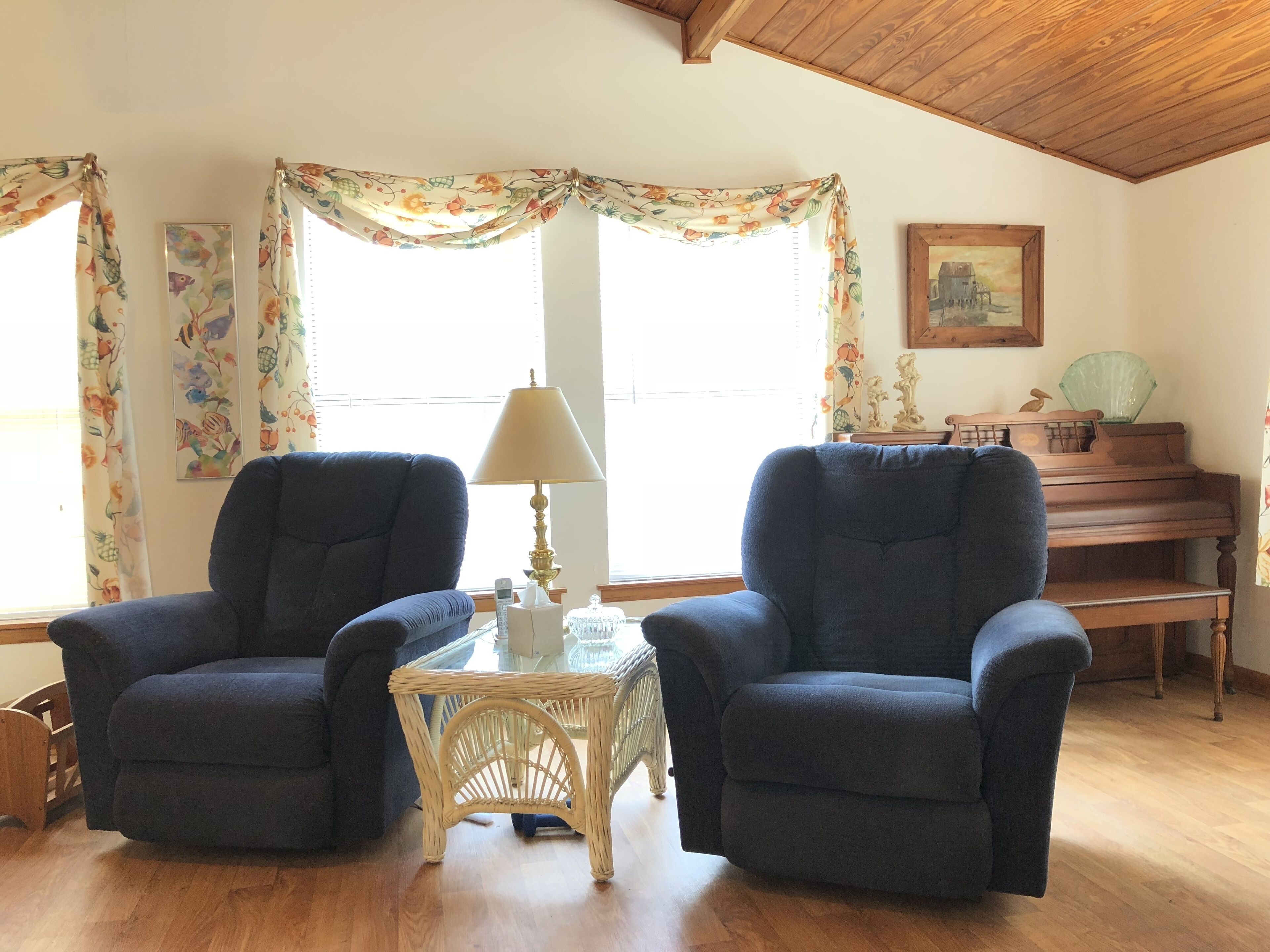 A room with two armchairs, a small table with a lamp, a piano, and a framed picture on the wall.