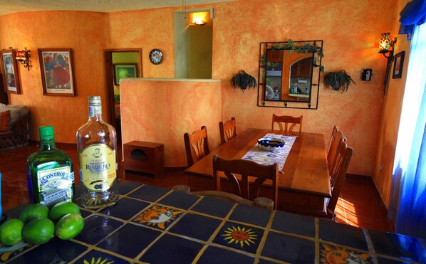 Un coin repas avec une table carrelée, des chaises et une bouteille de spiritueux. Des assiettes décoratives ornent le mur et un miroir est placé au-dessus de la table.