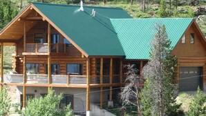 A two-story log cabin with a green metal roof, multiple windows, and a balcony. - Secluded Log Home with Mountain View (Granby)