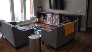 A living room with two grey sofas, a small white chair, a TV mounted on the wall, and a wooden cabinet with a sliding door.