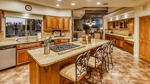 A spacious kitchen with wooden cabinets, a large island with bar stools, a built-in stove, and a window overlooking a scenic view. - Labor Day Available! Over the top!! Luxury, spacious, quiet family retreat. (Lake Havasu City)