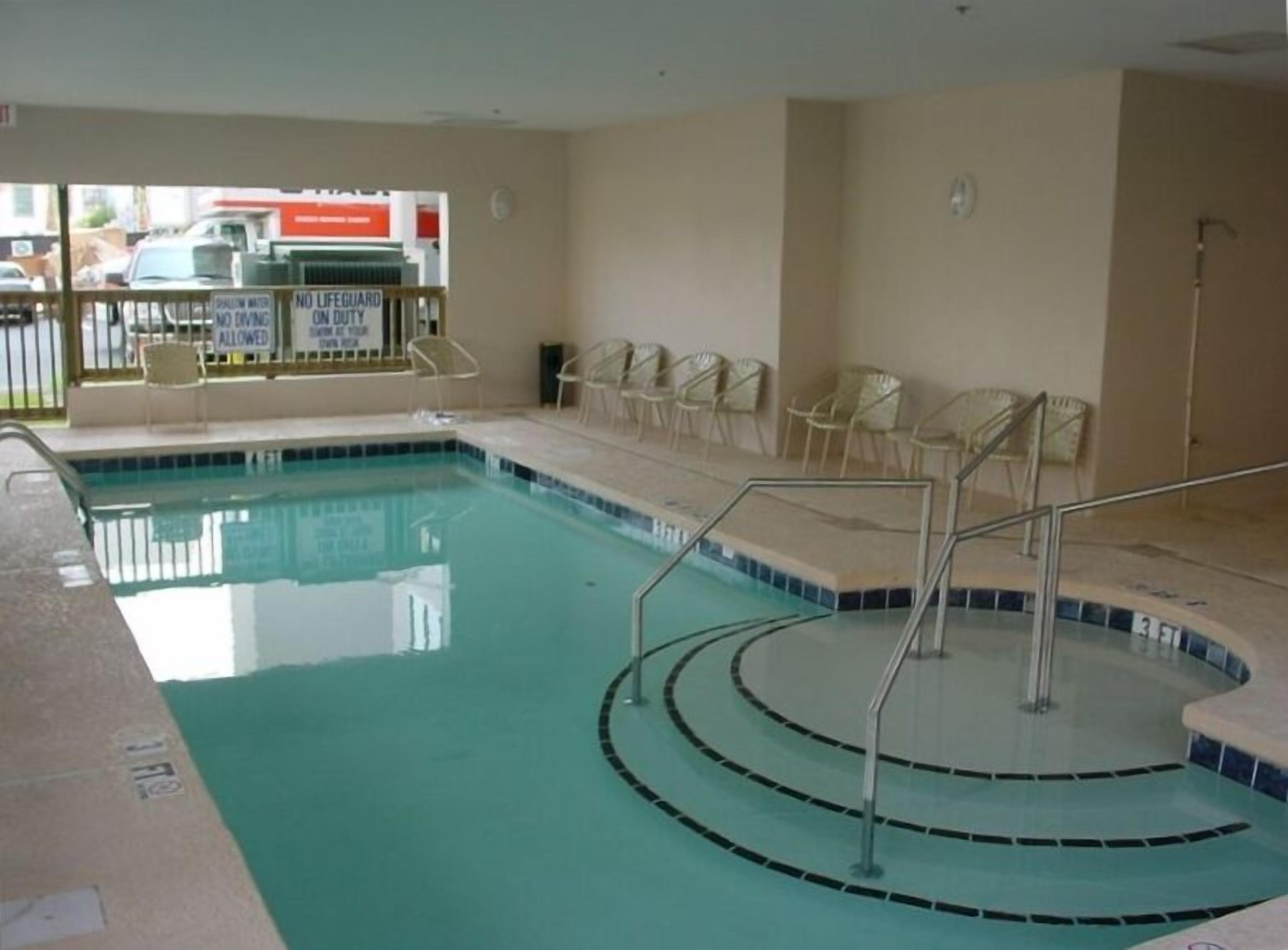 An indoor swimming pool with clear water, surrounded by white chairs and a lifeguard sign.