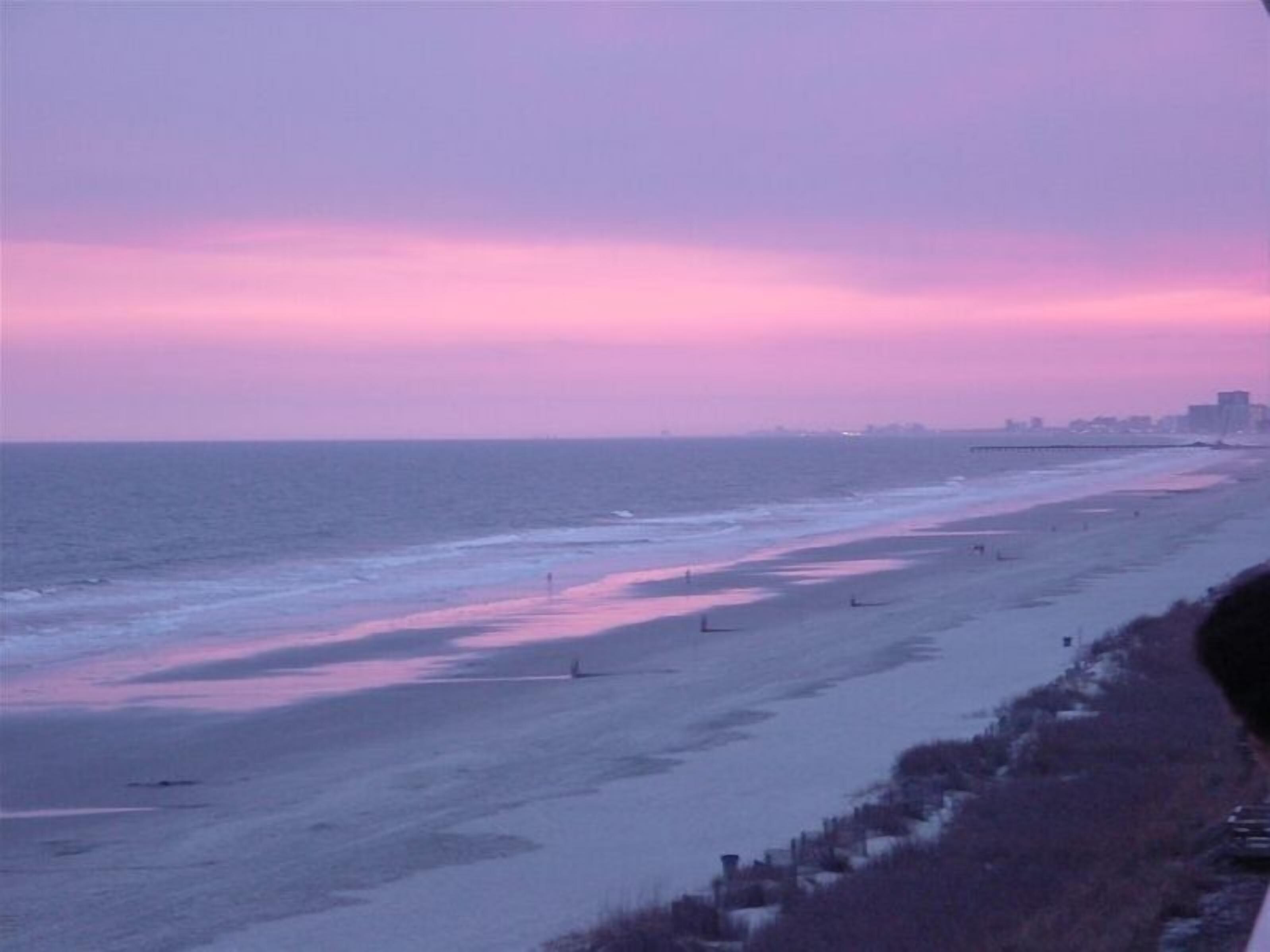 A beach with a calm sea and a pinkish sky, likely at sunset.