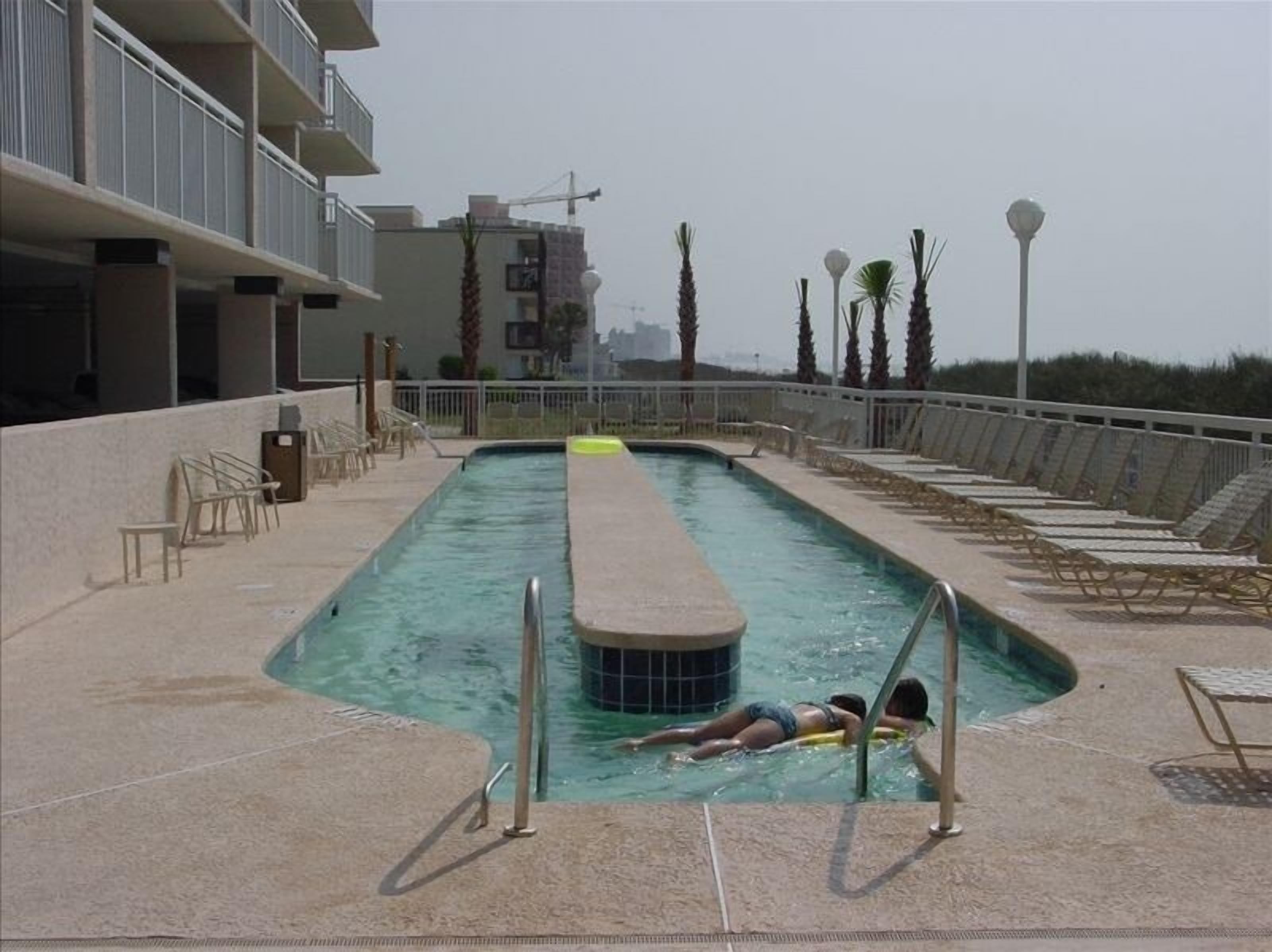 A swimming pool with a diving board, lounge chairs, and a view of the cityscape in the background.