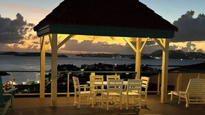 Un espace aménagé au bord de la piscine, avec un coin salon couvert et une vue sur la mer au crépuscule.