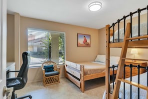 Ein kleines Zimmer mit einem Etagenbett, einem Einzelbett, einem Korbstuhl, einem Schreibtisch mit Stuhl und einem Fenster mit Jalousien.