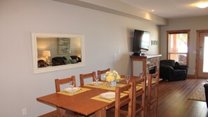 A dining area with a wooden table and chairs, a TV mounted on the wall, and a sofa in the background. - Experience a great family vacation at Casa Del Mila Oro ! (Osoyoos)