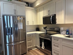A modern kitchen with stainless steel appliances, white cabinetry, and a black microwave. - Experience a great family vacation at Casa Del Mila Oro ! (Osoyoos)