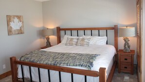 A neatly made bed with a wooden headboard, two bedside tables with lamps, and a maple leaf artwork on the wall. - Experience a great family vacation at Casa Del Mila Oro ! (Osoyoos)
