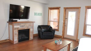 A living room with a fireplace, a black leather chair, a wooden coffee table, and a television mounted above the fireplace. - Experience a great family vacation at Casa Del Mila Oro ! (Osoyoos)