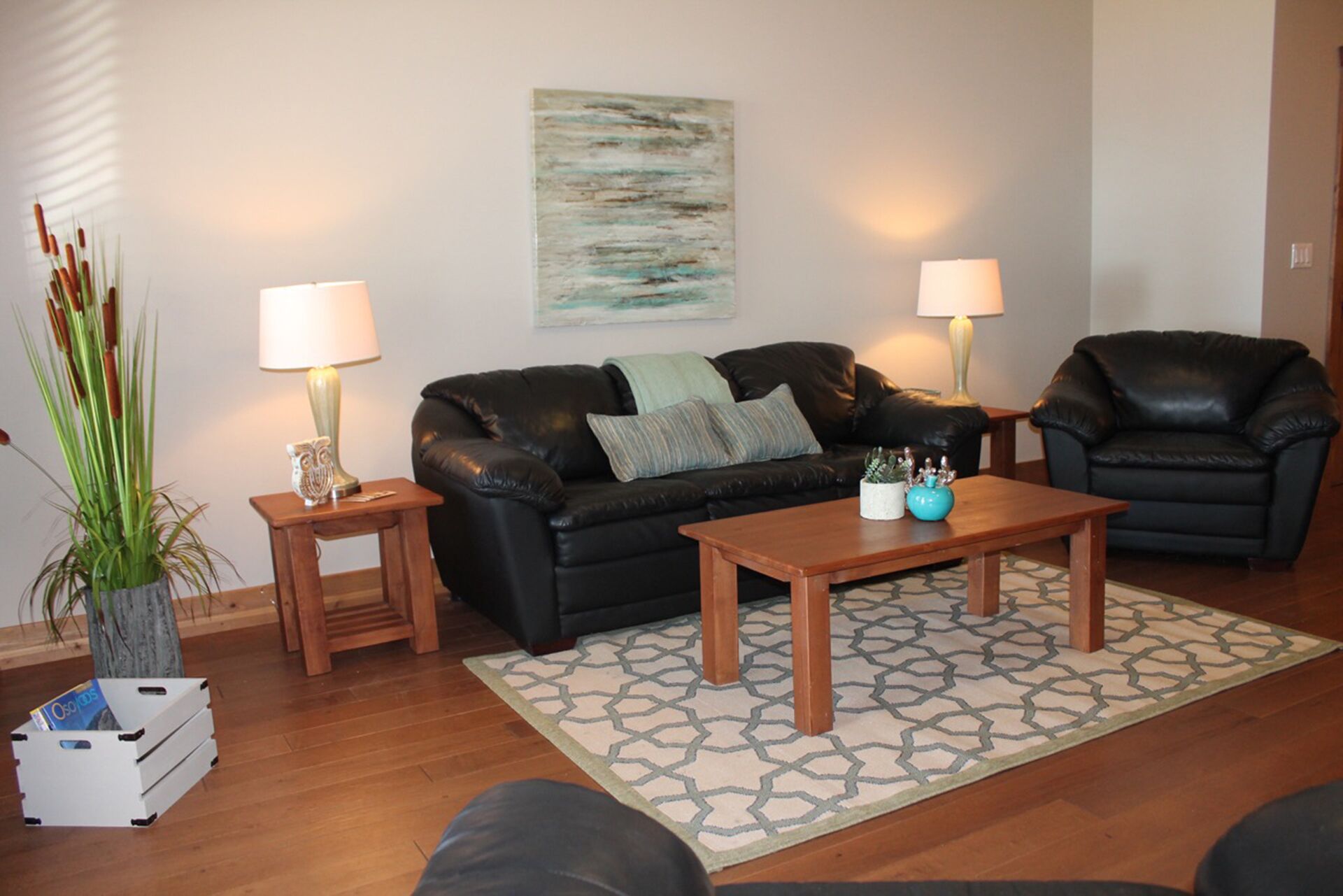 A living room with a black leather sofa, two wooden side tables, a coffee table, and a patterned rug.
