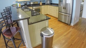 Une cuisine moderne avec des meubles blancs, des appareils en acier inoxydable, un îlot central et une poubelle.