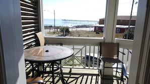 Un espace extérieur abrité, avec une table et des chaises, offrant une vue sur une jetée et une plage.