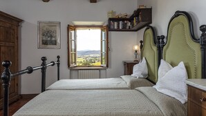 A bedroom with two beds, a window with a view, a bookshelf, and a wooden cabinet. - Traditional Tuscan farmhouse with stunning views & air conditioning (Siena)